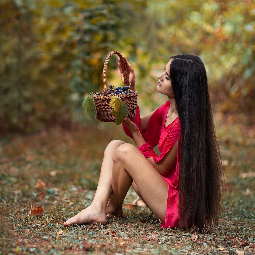 Sesja zdjęciowa w Lublinie i okolicach – 8 miejsc na plener fotograficzny 3 Portret kobiety siedzącej na trawie z koszem owoców w czerwonej stylizacji, plenerowa fotografia fashion z naturalnym światłem i miękkim tłem