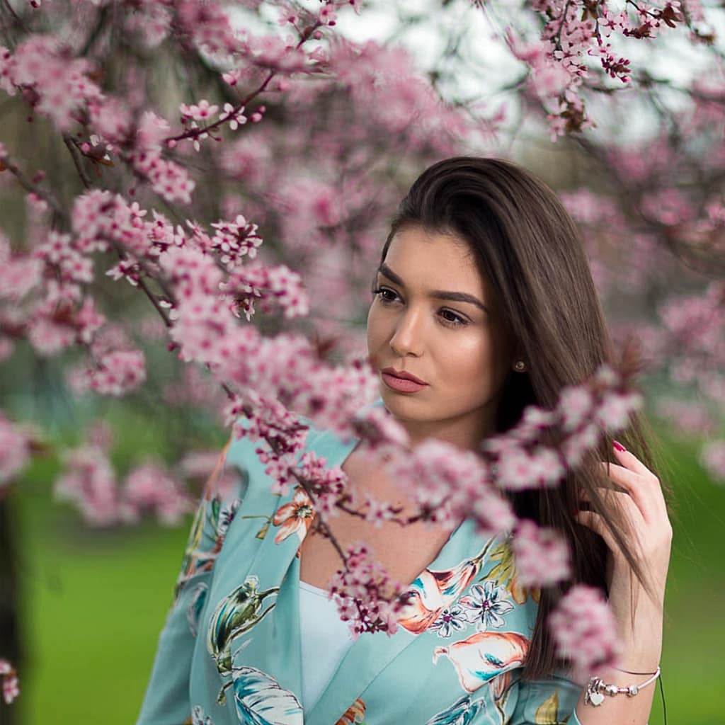 Sesja zdjęciowa w Lublinie i okolicach – 8 miejsc na plener fotograficzny 2 Artystyczny portret kobiety wśród kwitnących różowych gałęzi drzew owocowych, subtelna fotografia plenerowa beauty z delikatnym rozmyciem tła, pastelowe kolory i romantyczny klimat wiosennej sesji zdjęciowej