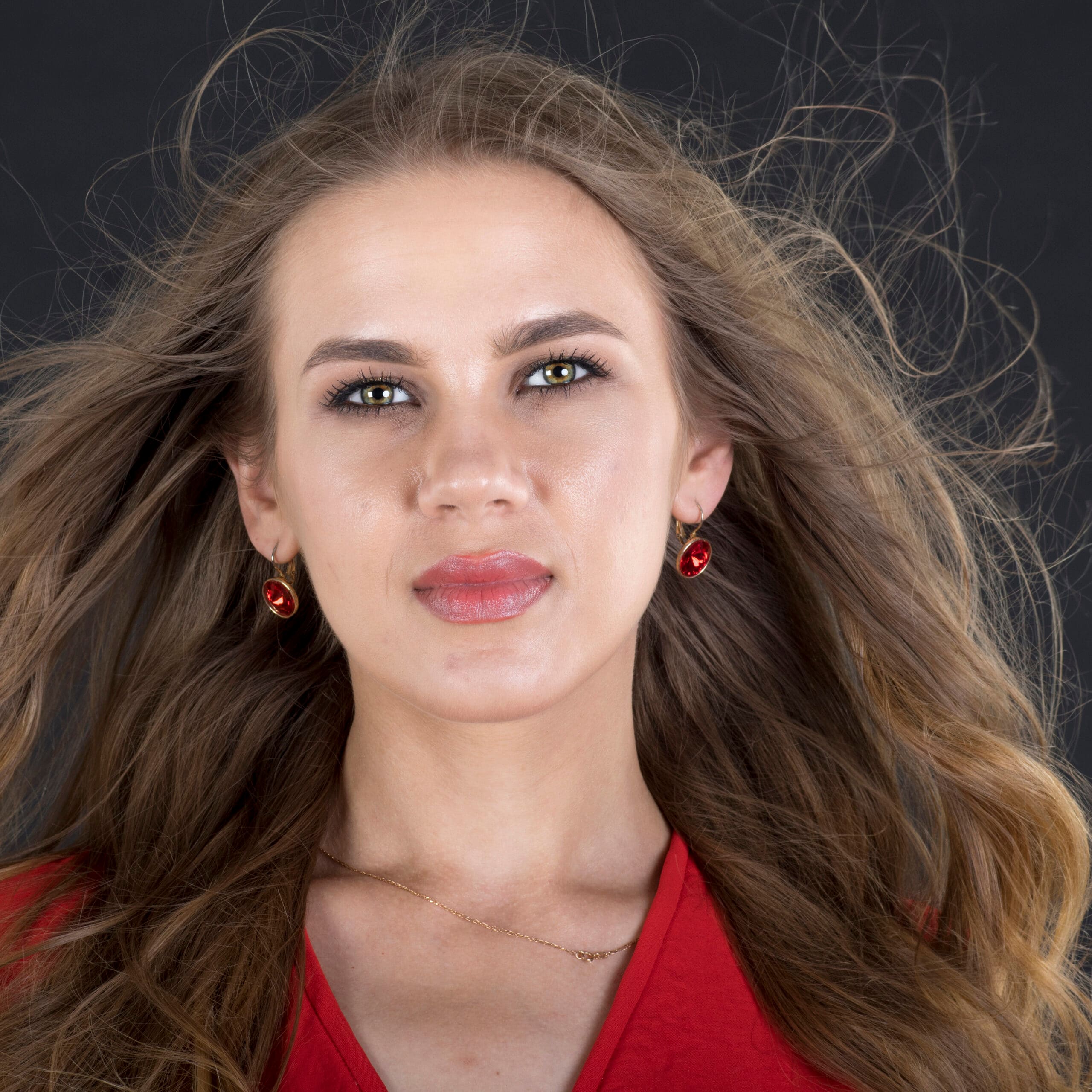 Psychologia portretu — dlaczego sesja portretowa zaczyna się od człowieka, nie od aparatu 11 Studyjny portret kobiety z falującymi włosami i czerwonymi kolczykami na ciemnym tle, fotografia beauty z wysoką szczegółowością skóry, naturalnym światłem i elegancką minimalistyczną kompozycją kadru