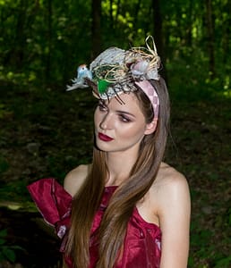 Portret z sesji bajkowo baśniowej w lesie Portret modelki w czerwonej sukni i ozdobnym kapeluszu podczas sesji zdjęciowej w lesie