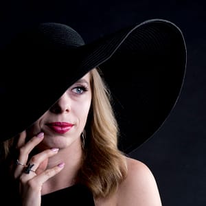 Elegancki portret kobiety w dużym czarnym kapeluszu, subtelne światło studyjne, minimalistyczne tło i klasyczny styl fotografii fashion beauty