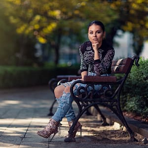 Fashion lifestyle park Dziewczyna siedząca na ławce w parku w modnej stylizacji jeansowej i botkach, plenerowa sesja lifestyle, fotografia fashion z rozmytym tłem bokeh