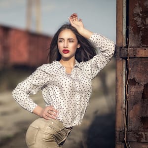 Sesja fashion industrial Portret kobiety w jasnej koszuli w drobne serca pozującej przy industrialnej konstrukcji, stylowa sesja modowa plenerowa, naturalne światło, fotografia portretowa lifestyle