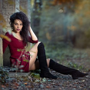 Sesja plenerowa – czerwona sukienka Portret kobiety w czerwonej sukience i czarnych kozakach siedzącej w leśnym plenerze jesiennym, artystyczna fotografia modowa outdoor, naturalne światło i klimat lifestyle
