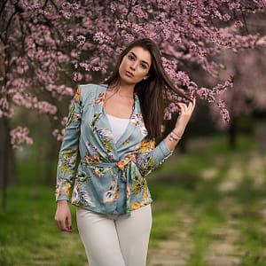 Wiosenna sesja pod kwiatami Portret kobiety w kwitnącym sadzie pod różowymi kwiatami, fotografia wiosenna fashion lifestyle z naturalnym światłem i pastelową kolorystyką plenerową